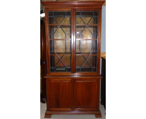 An early 20th century Georgian style mahogany full height bookcase with 2 leaded glass doors over double fielded panel cupboa