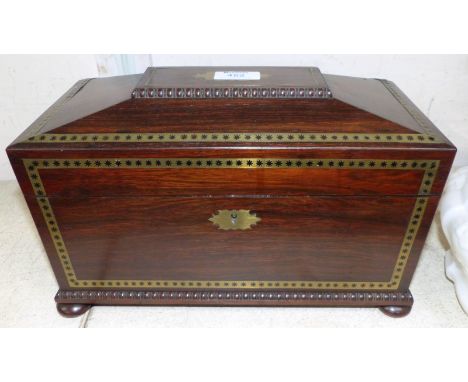 An early 19th century brass inlaid rosewood sarcophagus shaped tea caddy with ring handles, pad feet, and fitted interior