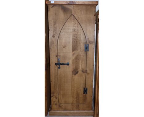 A rustic pine tall narrow cupboard enclosed by Gothic arch door