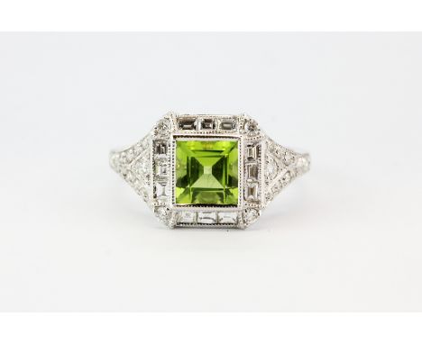 An art deco style 18ct white gold ring set with a centre princess cut bright peridot surrounded by princess, baguette and bri