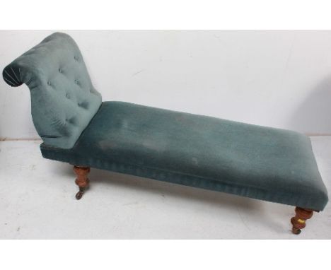 A chaise lounge with blue velvet upholstery, raised on turned supports to ceramic castors.