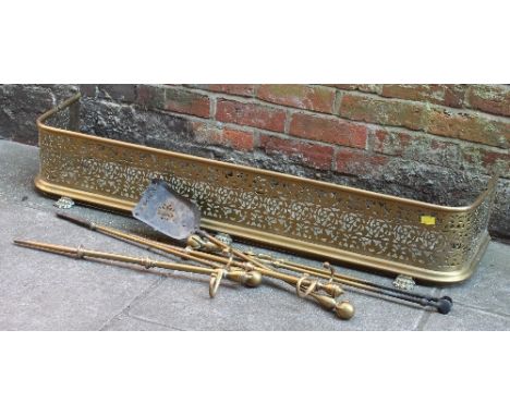 A collection of brass fire tools and a pierced brass fire surround with paw feet.