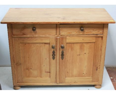 A stripped and waxed pine cupboard, with two frieze drawers above a pair of cupboard doors enclosing a shelf, raised on bun f