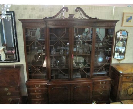 A CHIPPENDALE STYLE MAHOGANY BREAKFRONT BOOKCASE the scroll pierced pediment and blind fret frieze with astragal glazed doors