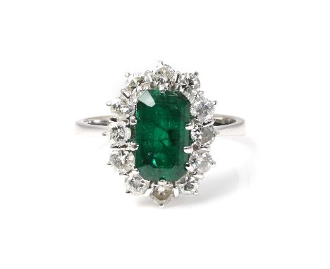An emerald and diamond cluster ring,  with a rectangular step cut emerald, 9.50 x 5.70mm, encircled by a surround of round br