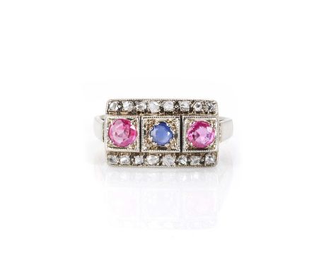 A three stone sapphire, ruby and diamond ring,  with a circular mixed cut sapphire, grain set in a square collet at the centr