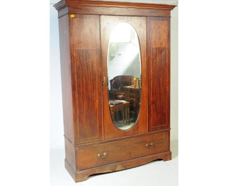 An early 20th century Edwardian mahogany inlaid wardrobe closet. Having a flared top, central oval mirror door flanked by inl