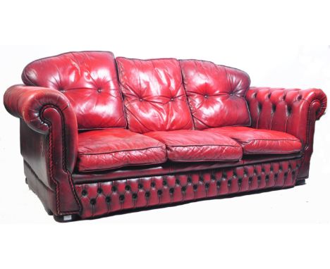 A vintage 20th Century antique style Chesterfield three seater sofa settee in a deep oxblood scarlet red leather having butto