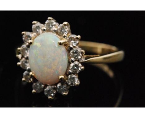 An 18ct opal and diamond cluster ring, oval opal cabochon bordered by fourteen brilliant cut claw set diamonds to a plain tap