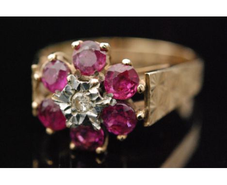 A 9ct ruby and diamond cluster ring, central diamond within a six stone ruby surround to wide sunburst shoulders, ring size N