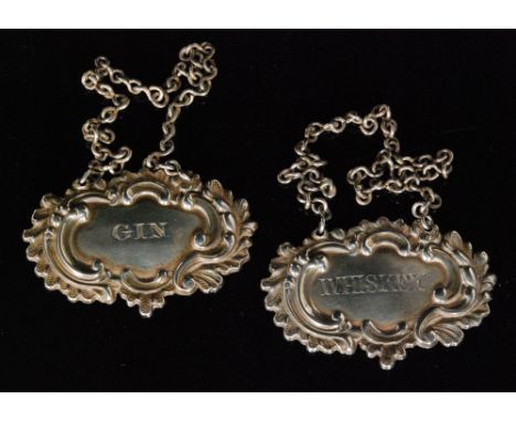 A pair of William IV hallmarked silver decanter labels for Gin and Whiskey, each with leaf and scroll embossed border decorat