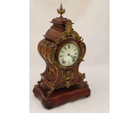 A stained mahogany mantle clock in the Rococo style, the white dial with Roman numerals denoting hours and in a balloon shape