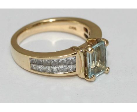 A 14 carat gold ring claw set with a central rectangular aquamarine and channel set with twenty four graduated princess cut d