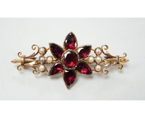 A late Victorian yellow metal, foil backed garnet and split pearl set flower head bar brooch, 55mm, gross weight 7.9 grams.