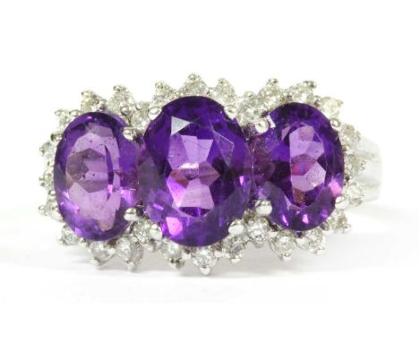 A 9ct white gold amethyst and diamond triple cluster ring, a graduated row of oval mixed cut amethyst, with surround of brill