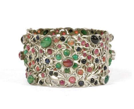 A silver hinged emerald, ruby and sapphire set bangle, pierced foliate motif bangle grain and rub set throughout with cabocho