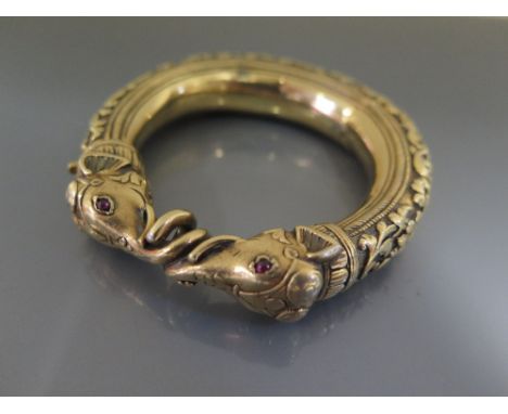 An Indian Silver Gilt Hinged Bangle decorated with elephant masks with entwined trunks and cabochon ruby eyes and with floral