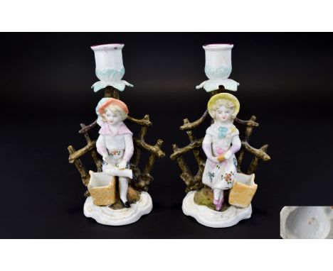 Pair of German Figural Candlesticks and Match Holders, a girl and a boy, each standing in front of a stylised tree trunk, whi