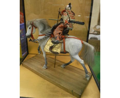 A model of a Japanese Samurai Warrior on horseback housed in a four-sided glass case, together with a Chinese embroidered cap