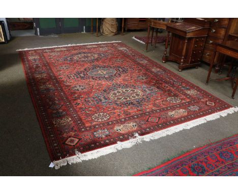 A Machine Made Carpet of Caucasian Design, the terracotta field with three stepped medallions enclosed by borders of geometri