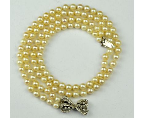 A two row pearl necklace, 6-6.5mm cream pearls, strung knotted, on a bow clasp, set with single cut diamonds, stamped 14 ct, 