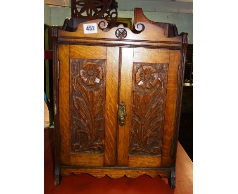 An early 20th century oak hanging smoker's cabinet, with floral carved panel doors, 32cm wide x 43cm high.