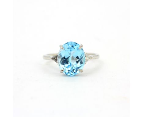 A 9ct white gold ring set with a large oval cut Swiss blue topaz and trillion cut diamond set shoulders, (M).