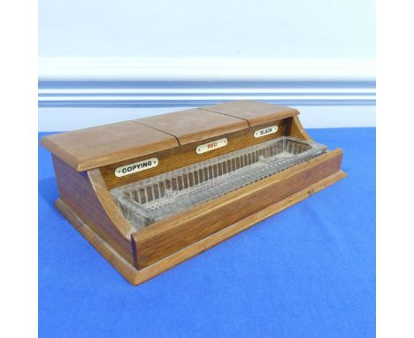A small oak hinged lid inkwell stand with three ceramic inkwells labelled 'Copying', 'Red' and 'Black' with a pressed glass p