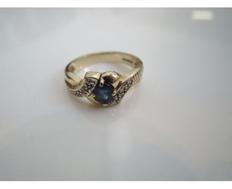 A dress ring, centred with an oval mixed-cut blue stone, the scrolling shoulders highlighted with six single-cut diamonds, in