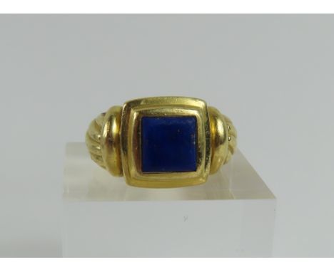 A heavy gold ring set with a lapis lazuli, the flat, square shaped stone in a stepped setting and with decoratively carved sh