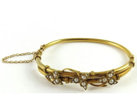 A Victorian hinged bangle, the front two bars crossed over each other with intertwined split pearl set leaves, marked '15ct',