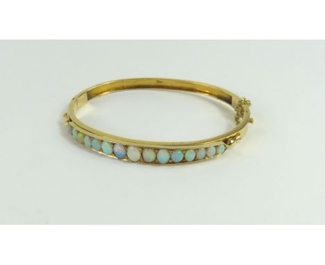 A Victorian or early 20th century white opal set hinged bangle, the fifteen cabochon cut stones graduated, 6.5cm internal dia
