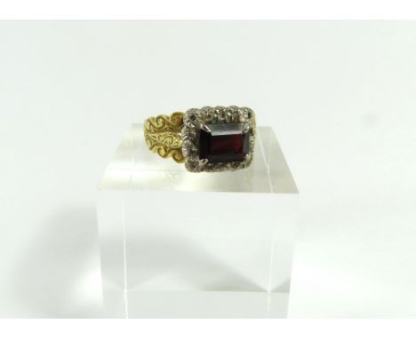 An unusual garnet and diamond cluster ring, the step cut garnet set lengthways with a row of round diamonds around, with heav