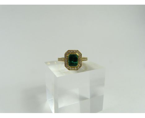 An 18ct gold emerald and diamond cluster ring, the step cut emerald in a rub over setting with beaded edge, surrounded by a r