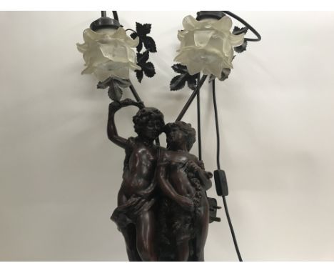 A Victorian style side lamp in the form of a young girl and boy with glass shades in The form of flower heads .