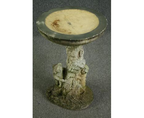 A composition stone pedestal bird bath, in the form of children playing around a tree trunk. H.60 Dia.45cm. 