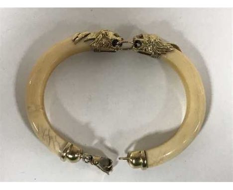 A 1920's two-piece ivory bangle, with 9ct gold mounts formed as lions with ruby set eyes