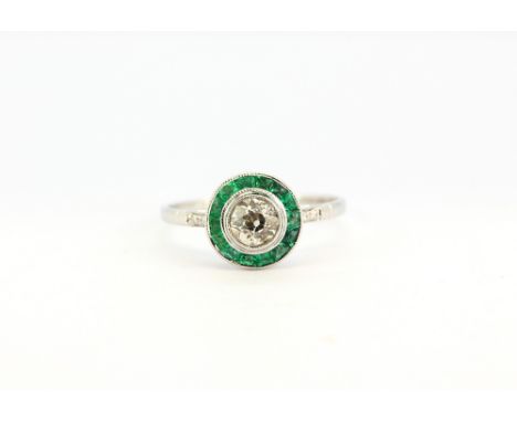 An 18ct white gold (stamped 18K) ring set with an old cut centre diamond surrounded by emeralds and diamond set shoulders, ap