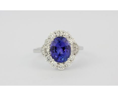 An 18ct white gold (stamped 750) cluster ring set with an oval cut tanzanite surrounded by brilliant and tapered baguette cut