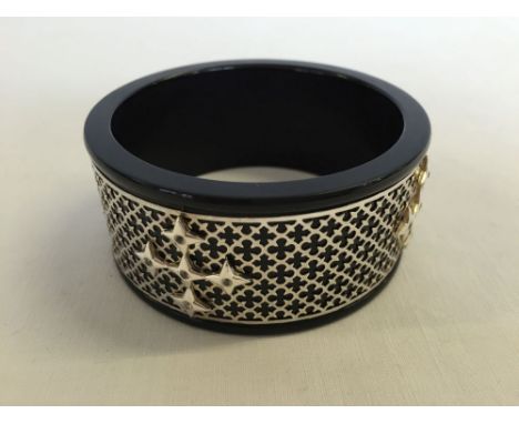 A black resin bangle with silver fretwork cladding set with white topaz stones.