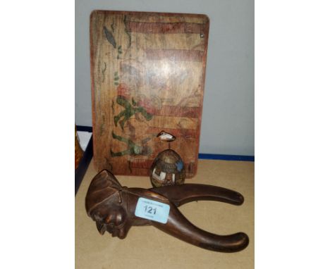 A carved Black Forest nutcracker in the form of a head, a painted board depicting gnomes and a carved egg 