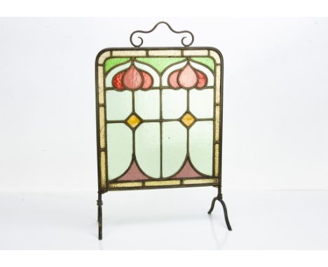 An Arts &amp; Crafts stained glass fire screen, the brass frame with astragal glazed central decoration of stylised three div