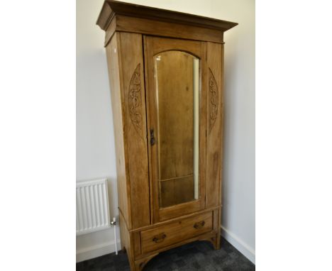 An Art Nouveau satin walnut single wardrobe, with mirrored bevelled arched door above a base drawer either side with carved s