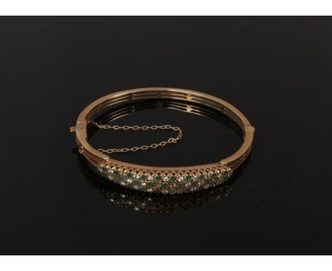 A 9ct gold openwork bangle pave set with emeralds and diamonds, gross weight 15.5 grams.