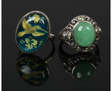 Two silver dress rings, one set with a large cabochon jade coloured stone, the other painted with a hummingbird, both size N.