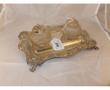 An Edwardian silver inkstand with shaped rectangular outline embossed with flower heads and C scrolls, centred by two cut gla