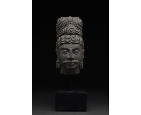 Ca. 200-300 AD A schist stone head of a Buddha. He is depicted with wavey hair gathered up in a topknot above a headband. His