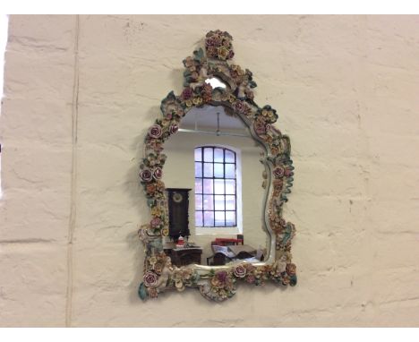 A wall mounted ceramic mirror with cherubic and floral decoration.