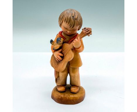 A vintage carved figure of a young boy playing a guitar with a bird perched on his arm. Artist carved name on the side. Anri 