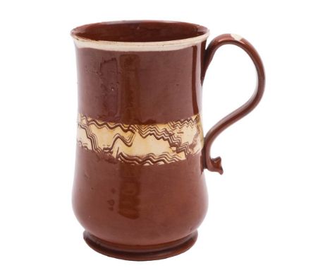 A Staffordshire glazed redware mug: of baluster form with strap handle and pinched terminal, decorated with a cream slip band